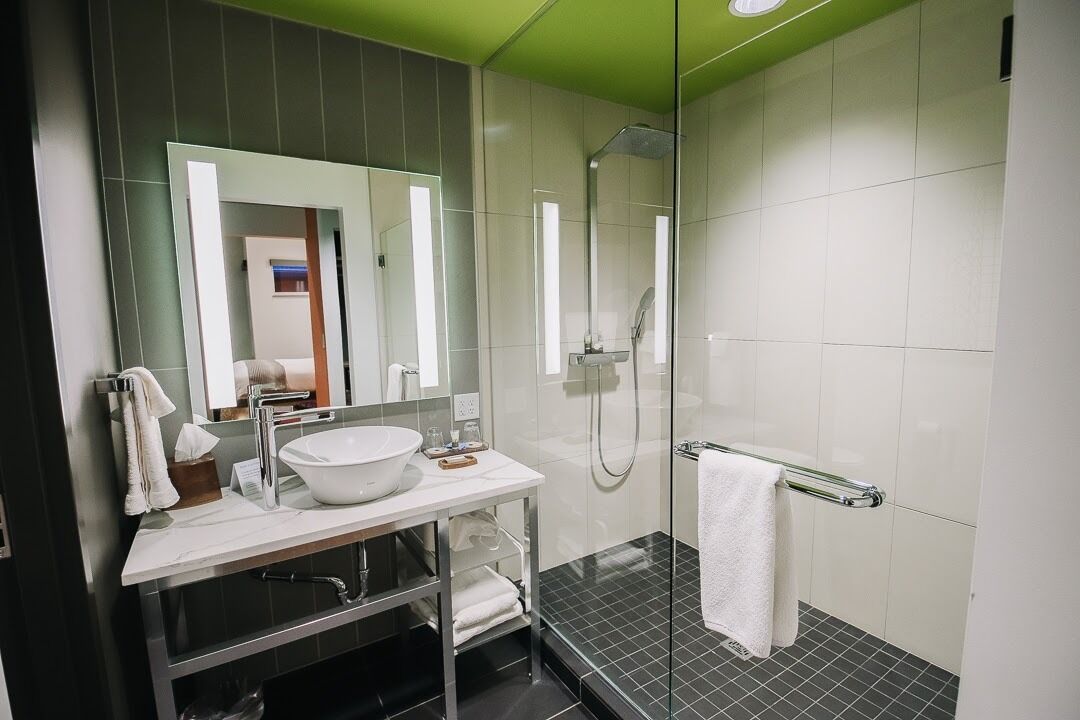 A modern bathroom with a large mirror, white sink, and a glass-enclosed shower area.