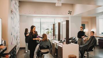A salon interior with a 'BLOW DRY BAR' sign, multiple hairdressing stations, and a large mirror.