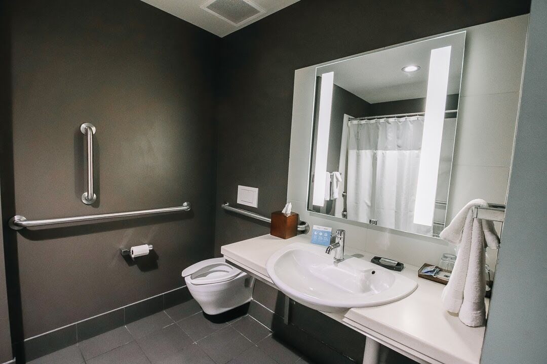 A modern bathroom with a white sink, mirror, and handrails.