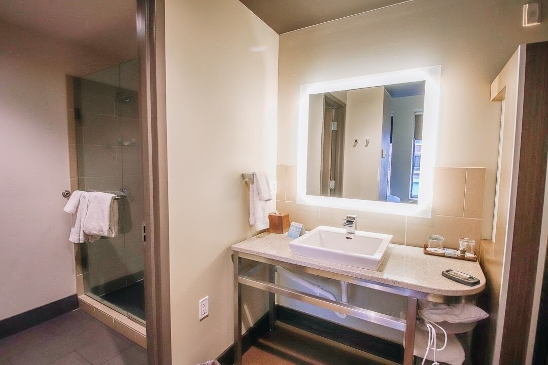 Ein modernes Badezimmer mit einer Duschkabine, einem weißen Waschbecken und einem Spiegel mit integrierter Beleuchtung.