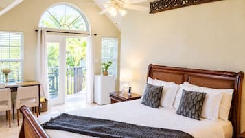 A bedroom with a large bed, a desk, and a balcony with a view of greenery.