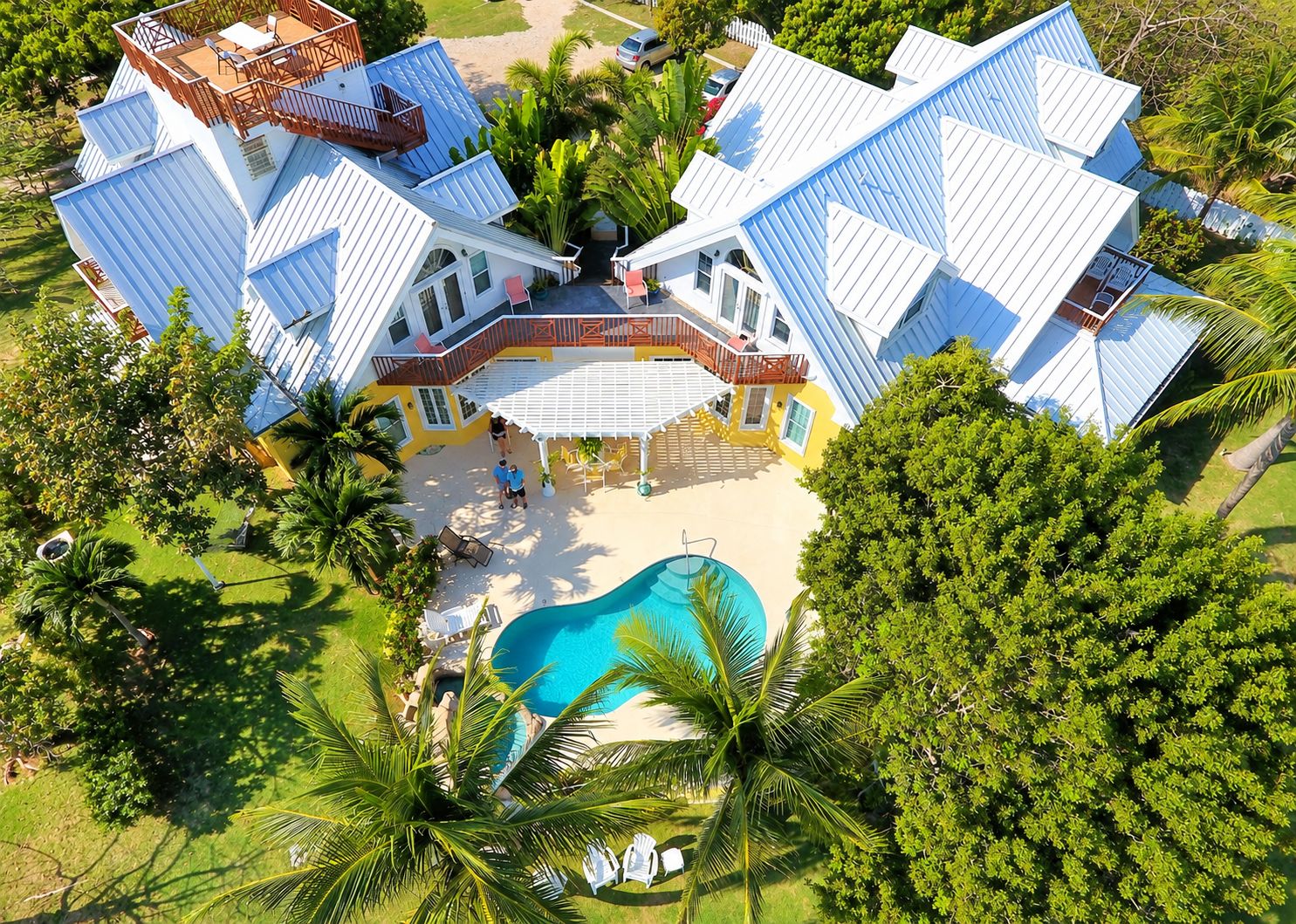 Una grande casa a più piani con piscina, circondata da palme e vegetazione.