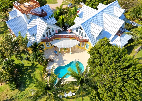 Una casa grande de varios pisos con piscina, rodeada de palmeras y follaje.