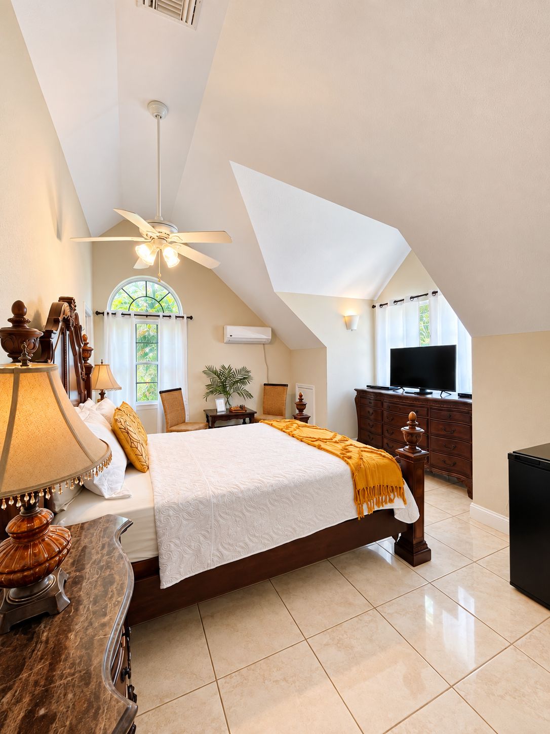 A bedroom with a bed, a desk, a chair, a television, and a ceiling fan.
