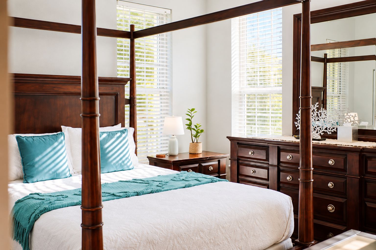 A four-poster bed with a wooden headboard, white bedding, and teal throw pillows.