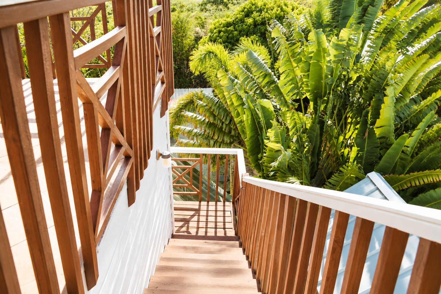 A wooden staircase leading to a balcony with a view of lush greenery.