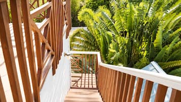 A wooden staircase leading to a balcony with a view of lush greenery.