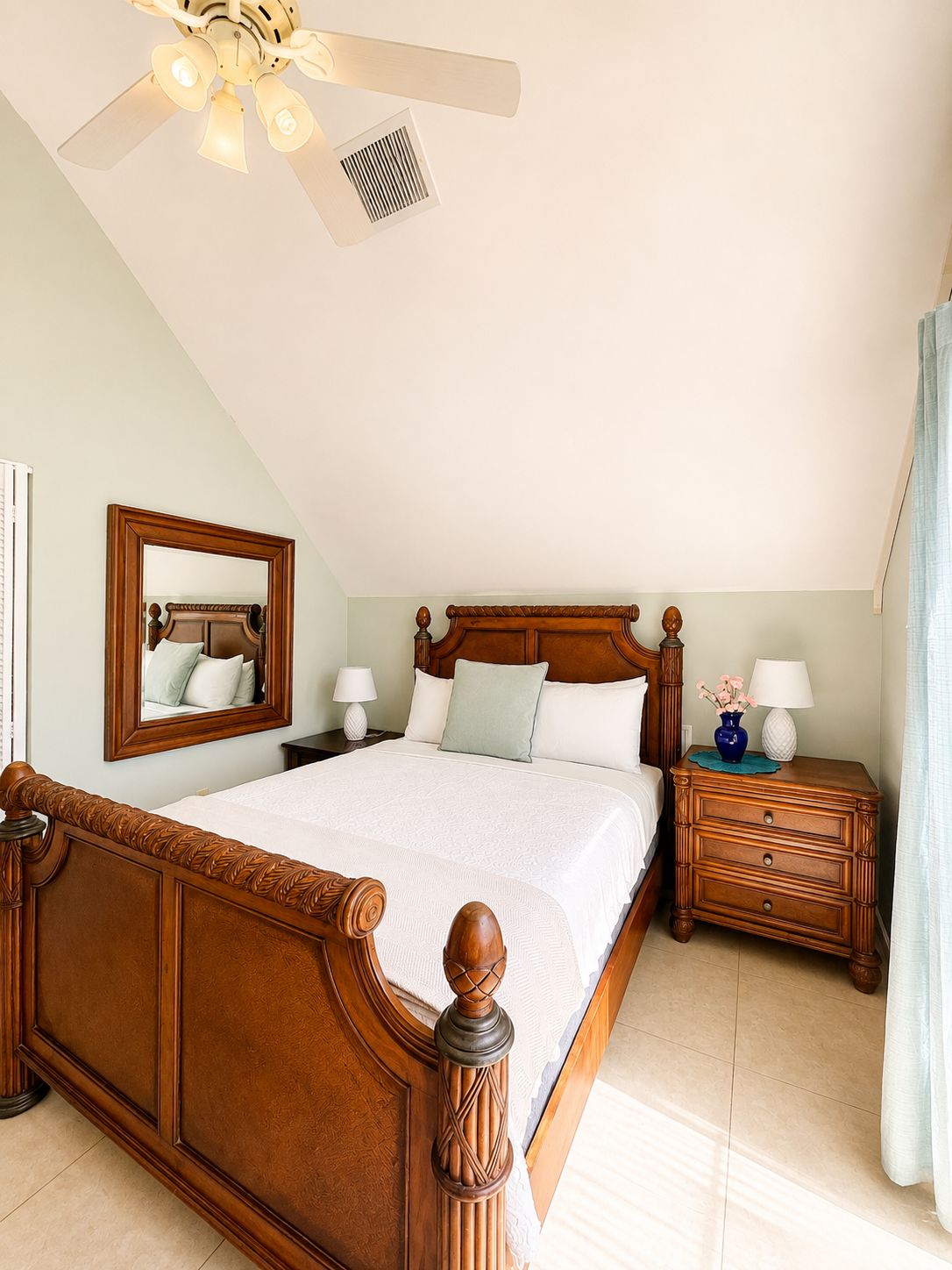 A bedroom with a wooden bed, a nightstand, a mirror, and a ceiling fan.