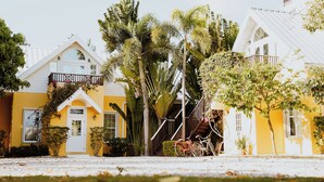 Une rangée de maisons jaunes aux contours blancs, entourées d’une végétation luxuriante et de palmiers.