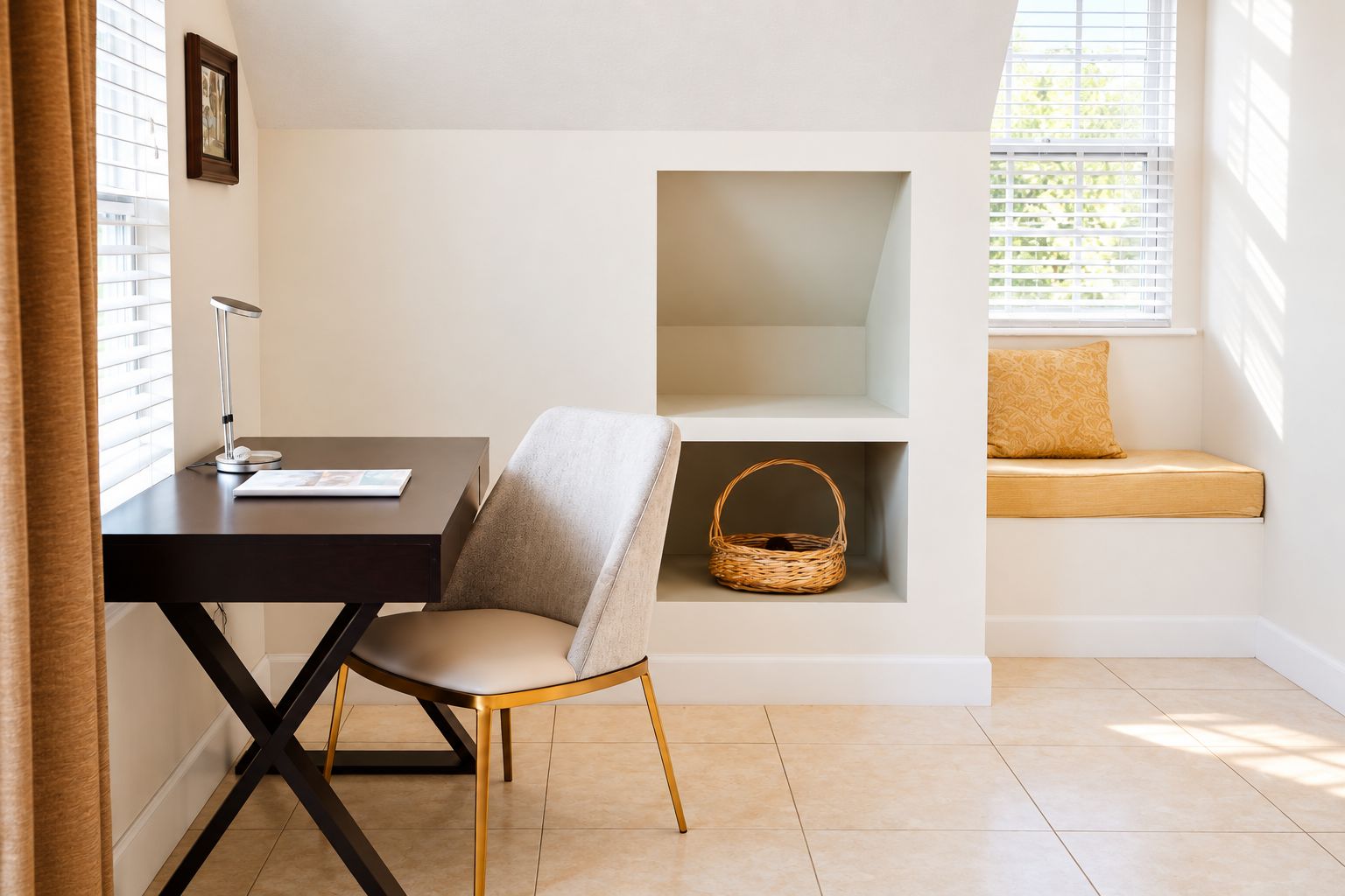 A room with a desk, chair, shelving unit, and a window seat with a cushion.