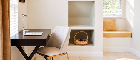A room with a desk, chair, shelving unit, and a window seat with a cushion.