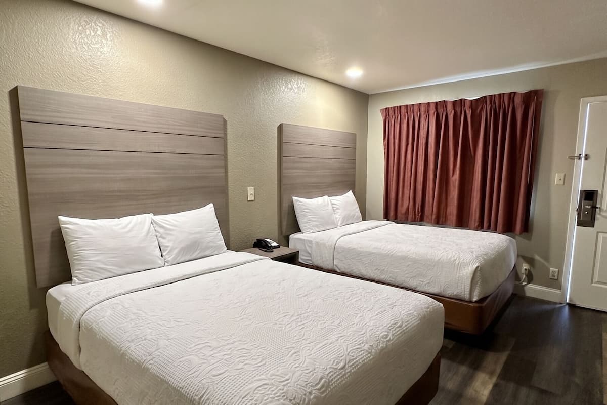 Quarto de hotel com duas camas, cabeceira de madeira, telefone e cortina vermelha.