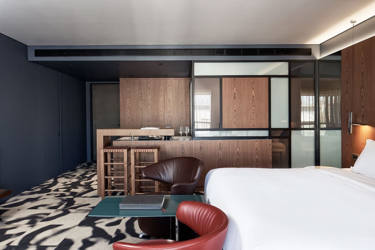 A modern hotel room with a bed, a desk, a chair, and a small table.