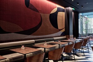 A modern restaurant with a geometric wall mural, cushioned seating, and a checkered floor.