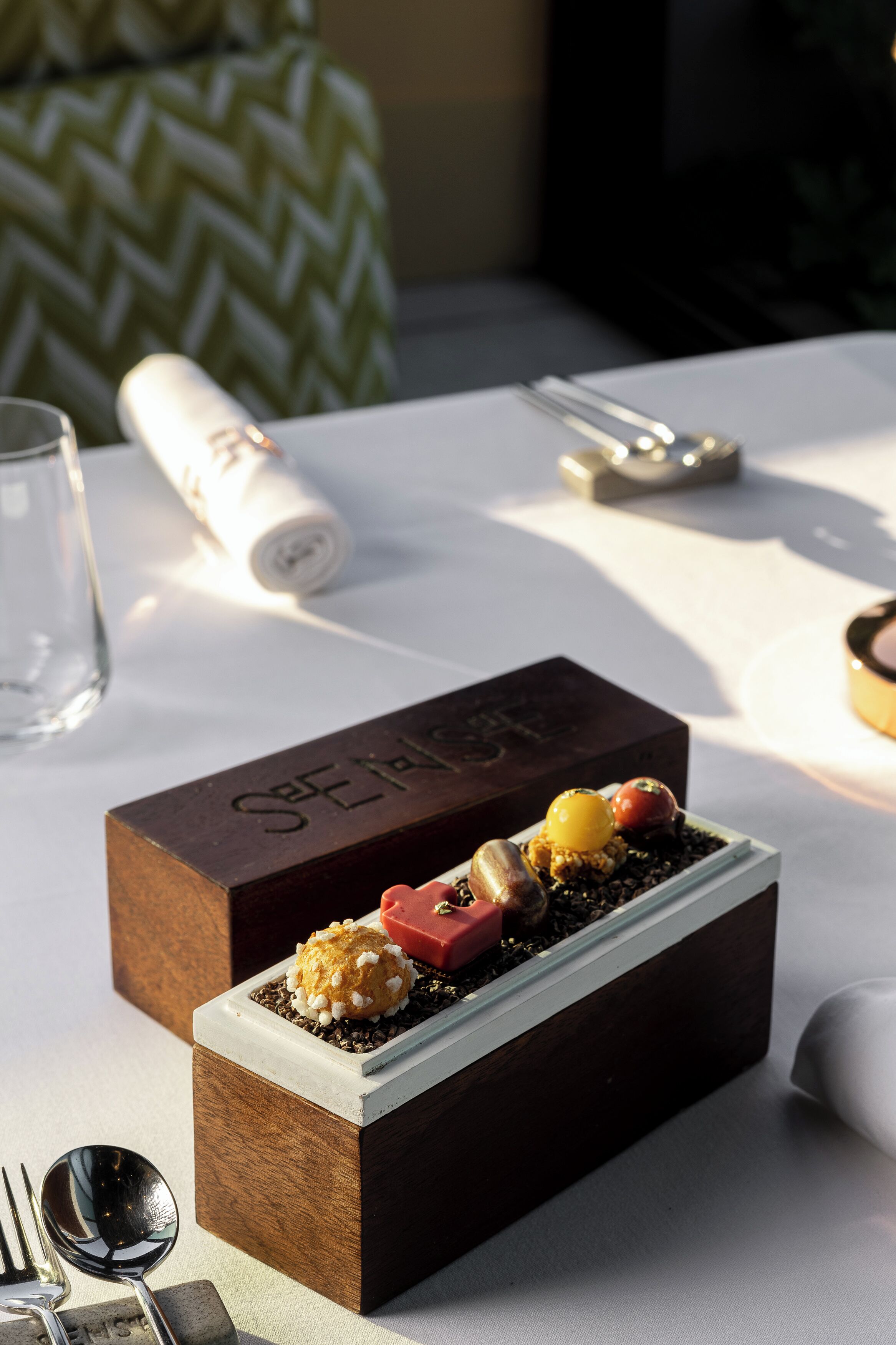 Un postre sobre una caja de madera con una placa, acompañado de una cuchara y un tenedor sobre una mesa.