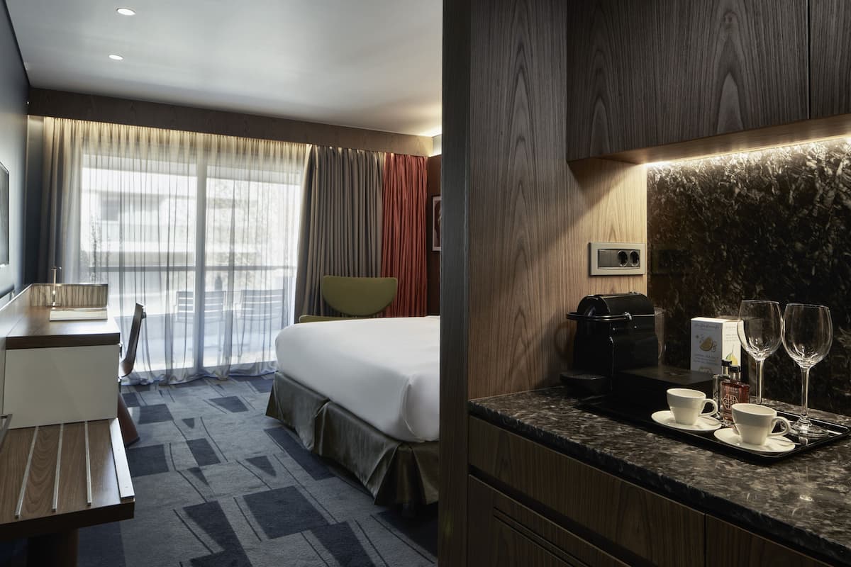 A hotel room with a bed, a desk, a chair, a coffee maker, and a tray with cups and glasses.