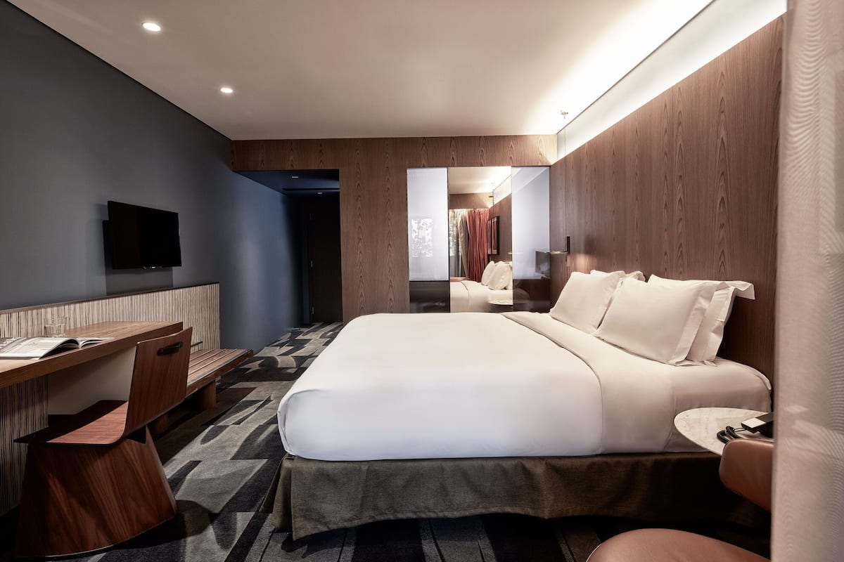 A modern hotel room with a bed, desk, chair, and television.