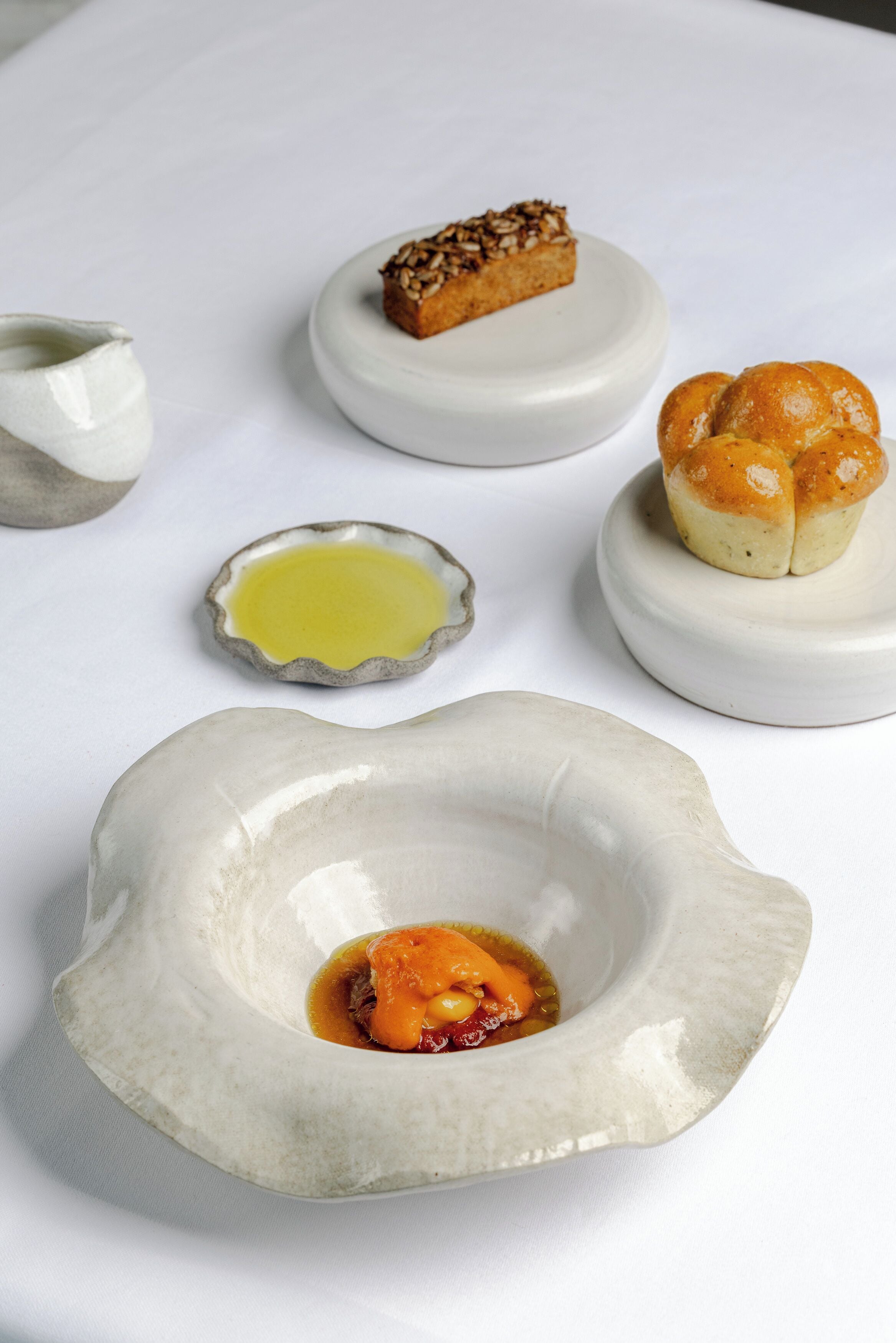 Een witte tafel met in het midden een schaal met vlees en saus, omringd door drie kleine schaaltjes met verschillende soorten eten.