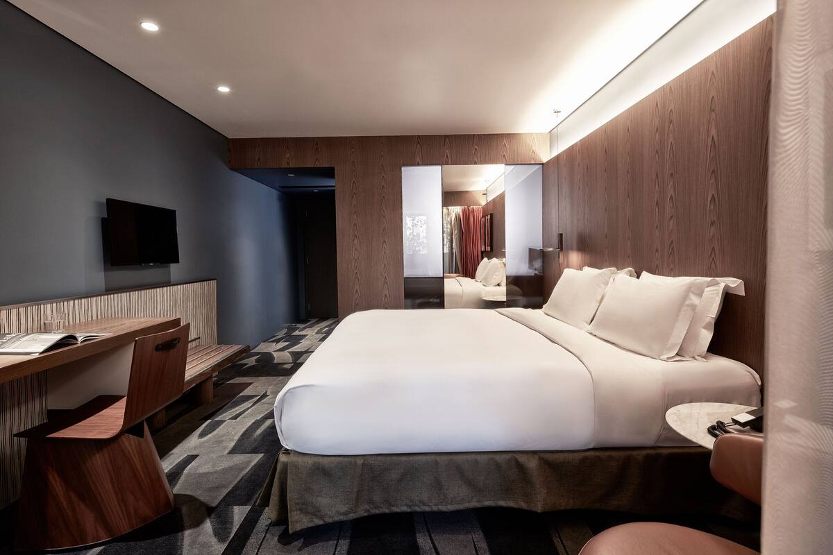 A modern hotel room with a bed, desk, chair, and television.