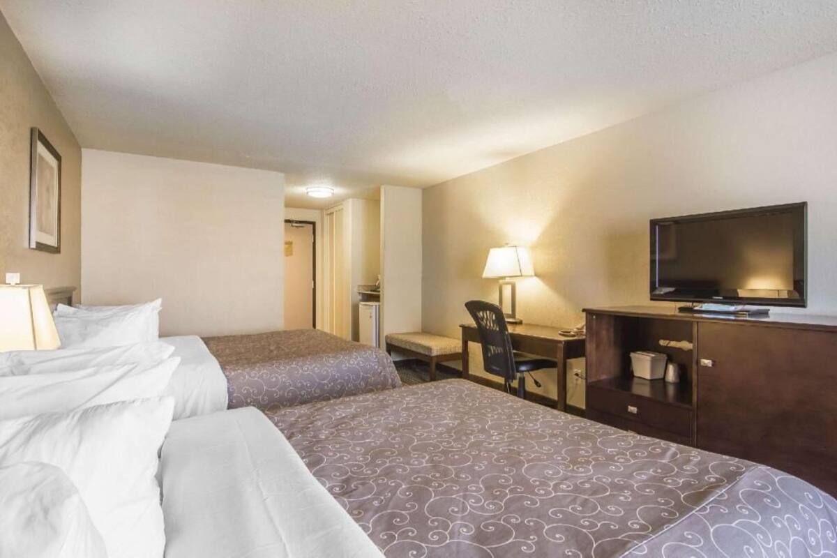 A hotel room with two beds, a desk, a chair, a television, and a lamp.