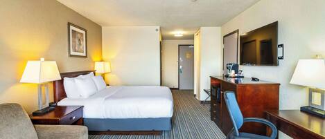 Habitación de hotel con cama, escritorio, silla, televisor y lámpara.