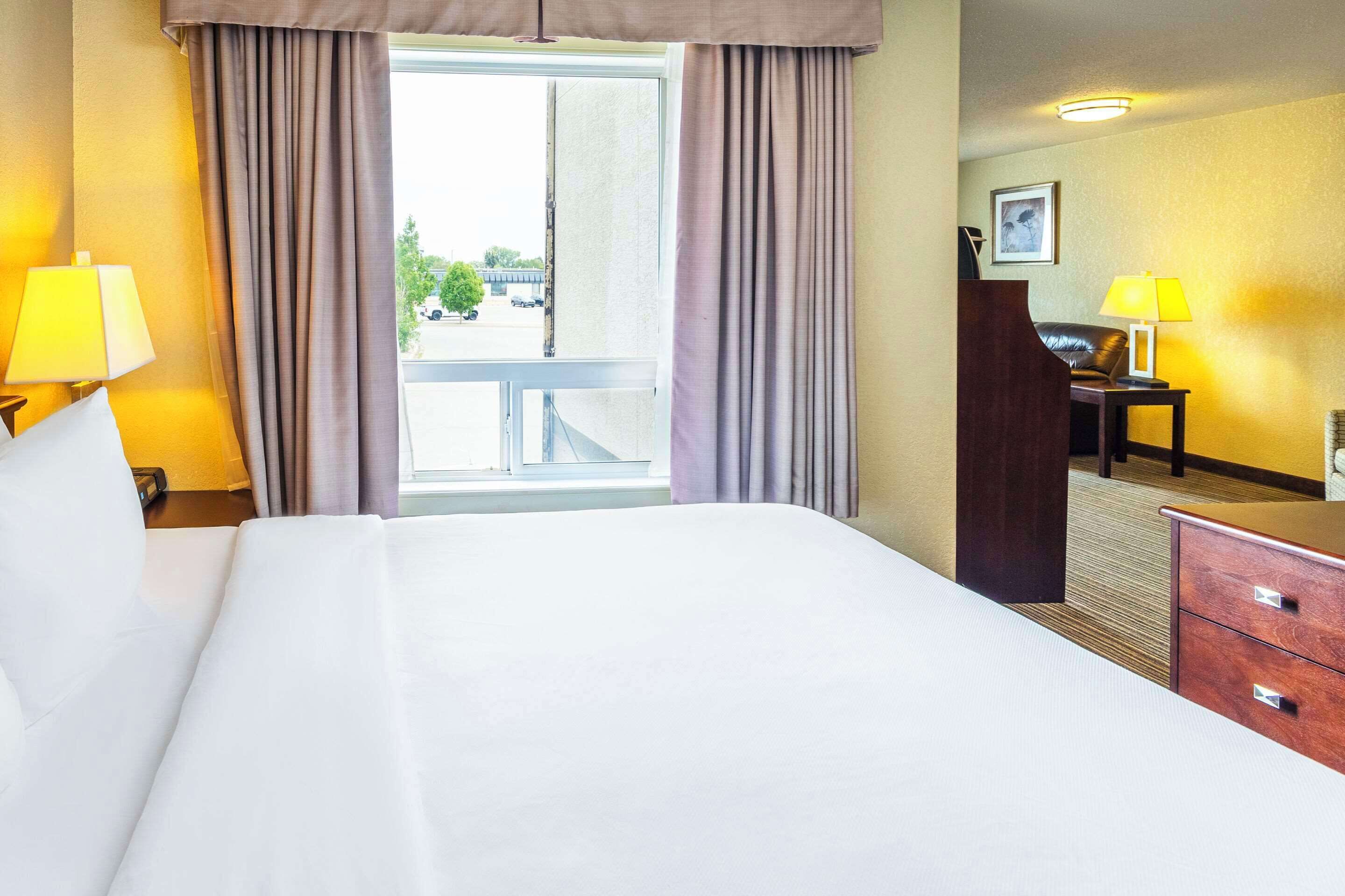 A hotel room with a large bed, two bedside lamps, a desk with a chair, and a view of the outside.
