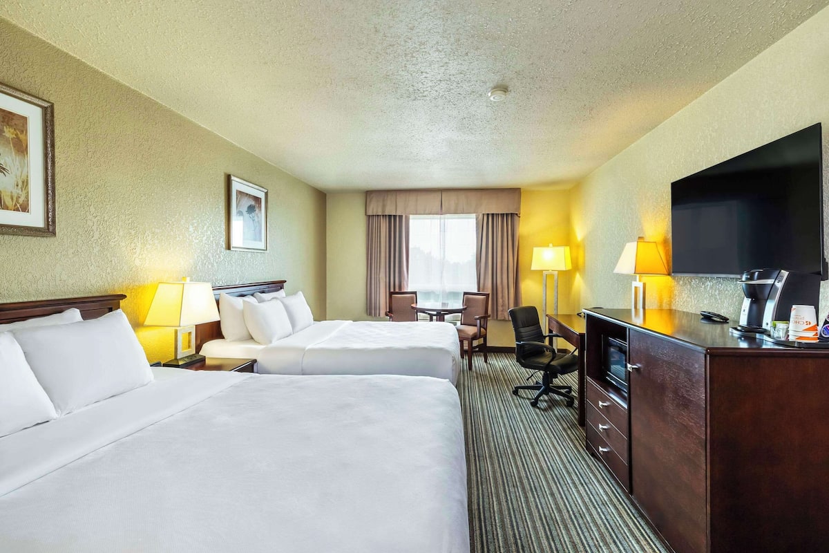 A hotel room with two beds, a desk with a computer, a TV, and a window with curtains.