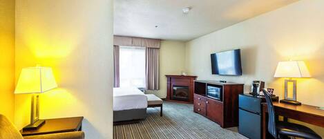Habitación de hotel con cama, escritorio, silla, televisión y chimenea.