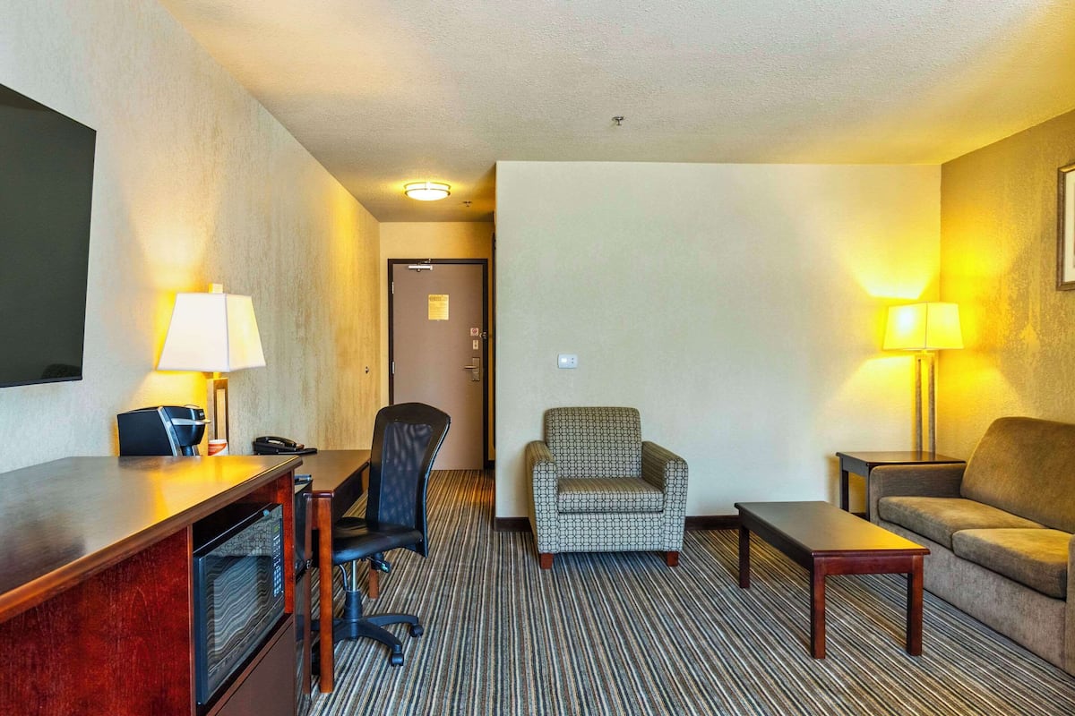A hotel room with a desk, chair, sofa, and two lamps.