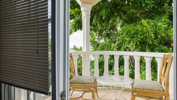 A covered outdoor seating area with wicker chairs and a small round table, surrounded by a white railing and lush greenery. - Khastle Khodero (Montego Bay)