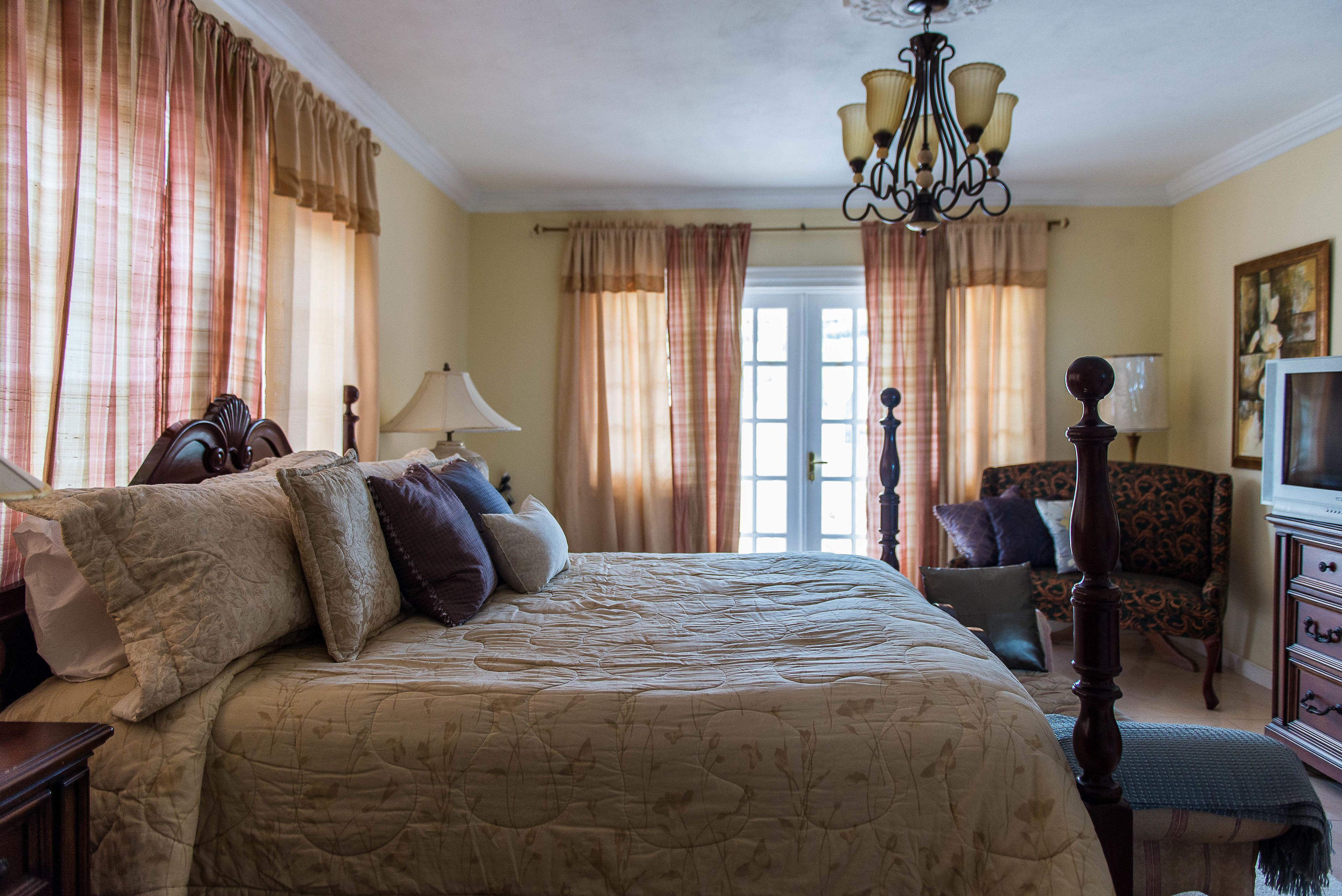 A bedroom with a large bed, a chair, a dresser, and a chandelier.