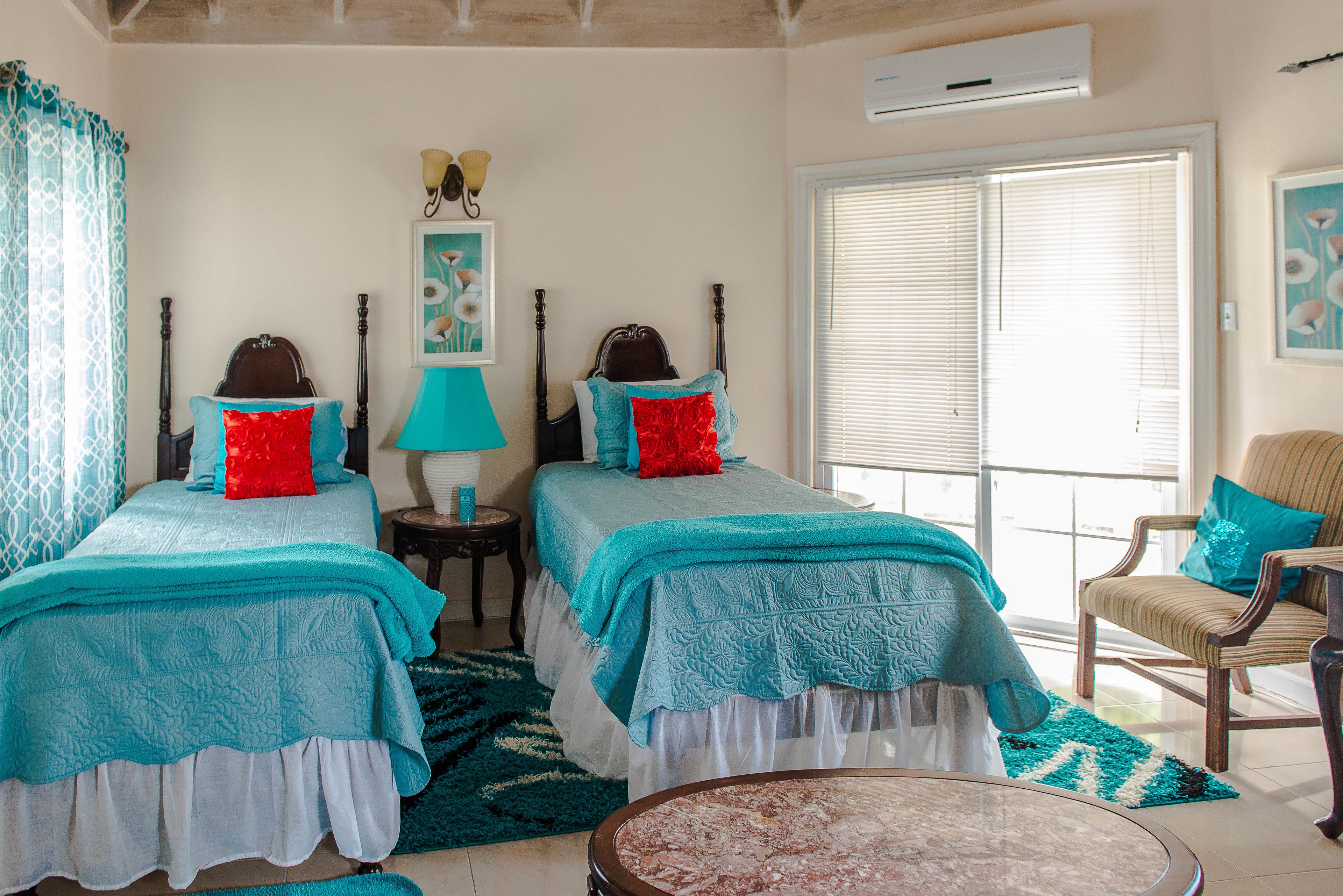 A bedroom with two beds, a round coffee table, a chair, and a window with blinds.