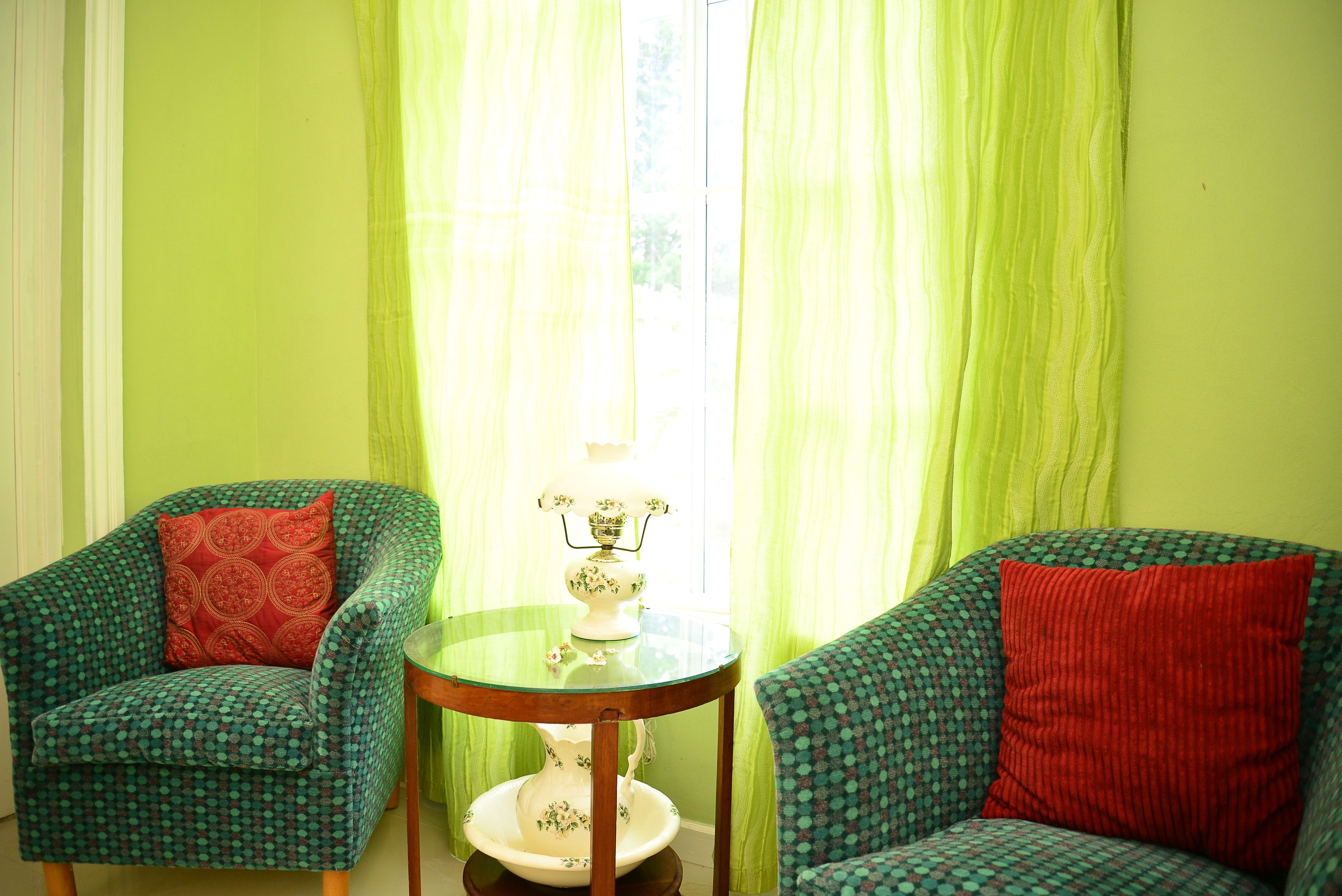 A room with two patterned armchairs, a small table with a decorative item, and sheer curtains.