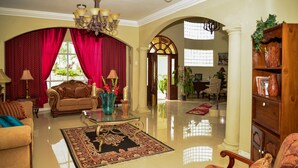 A spacious living room with a large red curtain, a chandelier, and a coffee table with a rug. - Khastle Khodero (Montego Bay)