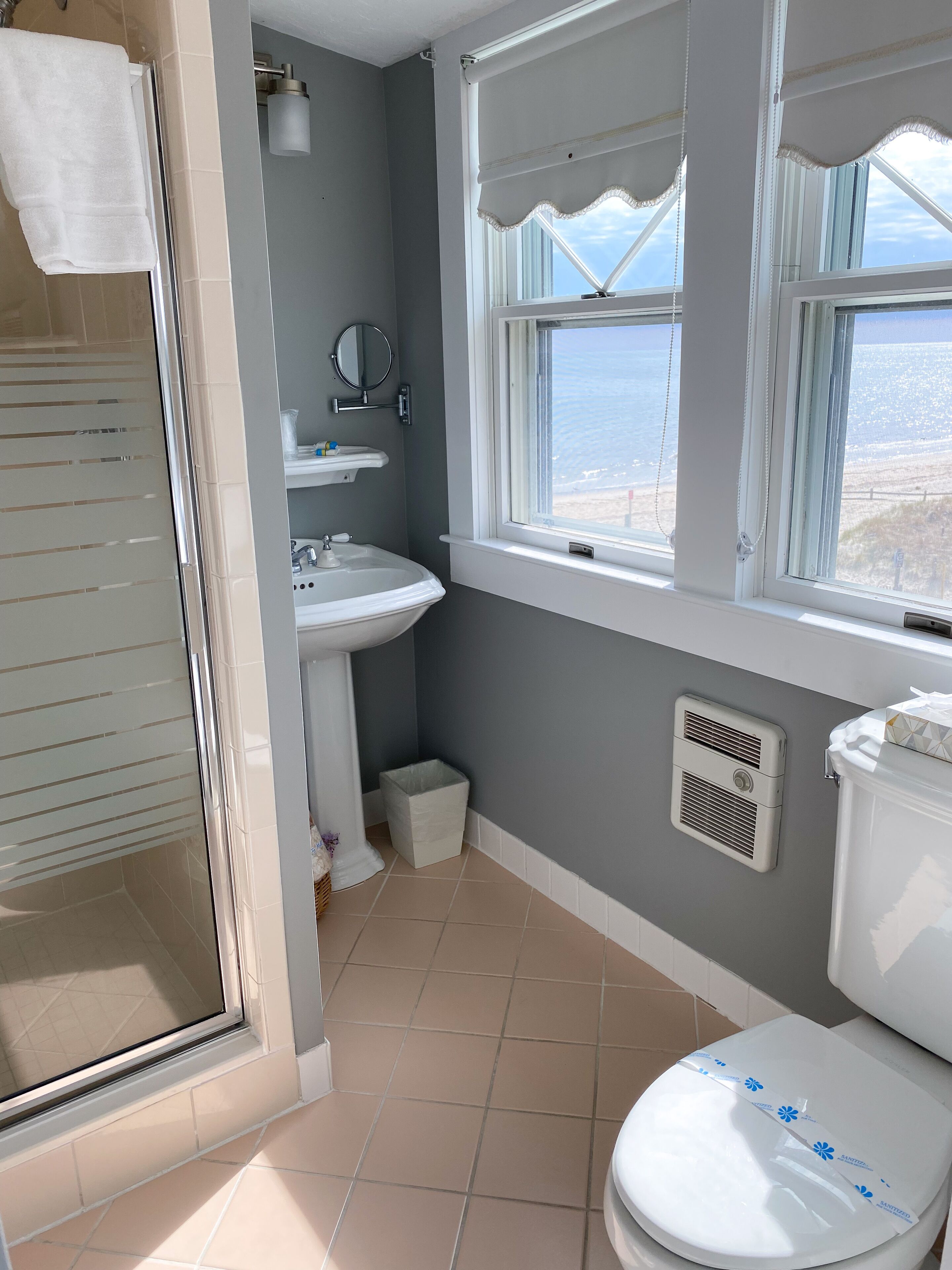 Un baño con inodoro, lavamanos y ducha. Hay una ventana con vista a la playa.