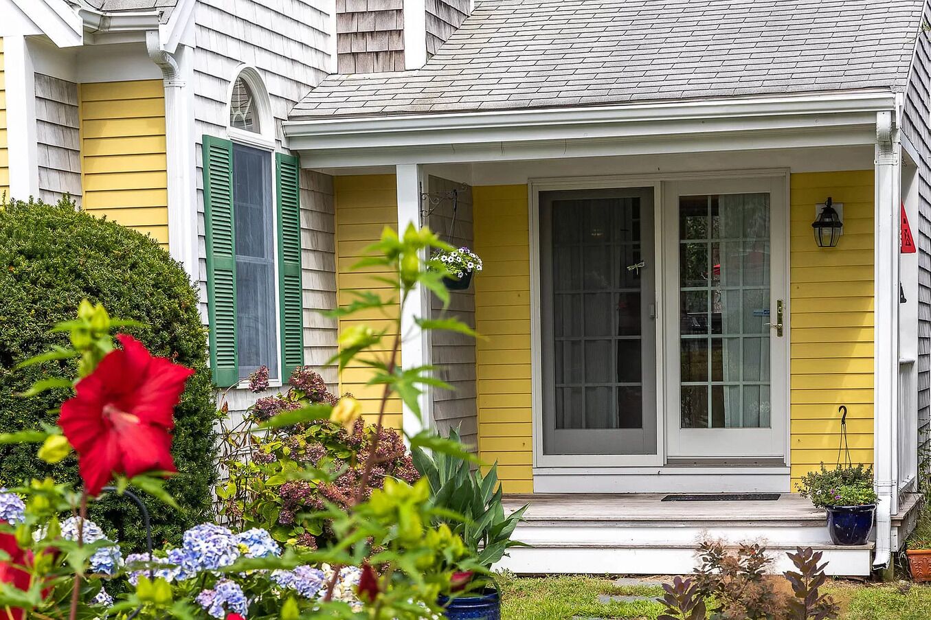 A yellow house with a front porch, green shutters, and a white door.