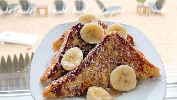 Een bord Franse toast met bananen, met uitzicht op het strand.