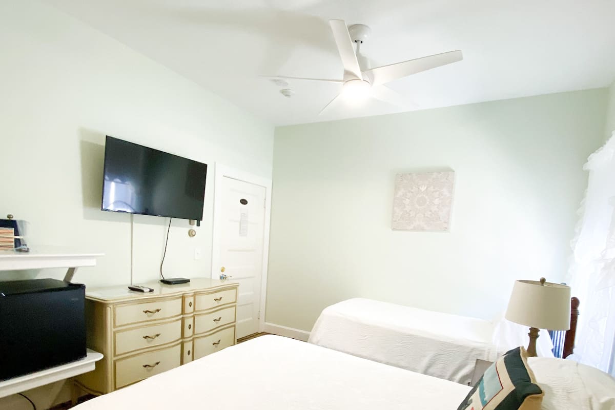 Een hotelkamer met een bed, een televisie, een bureau en een plafondventilator.