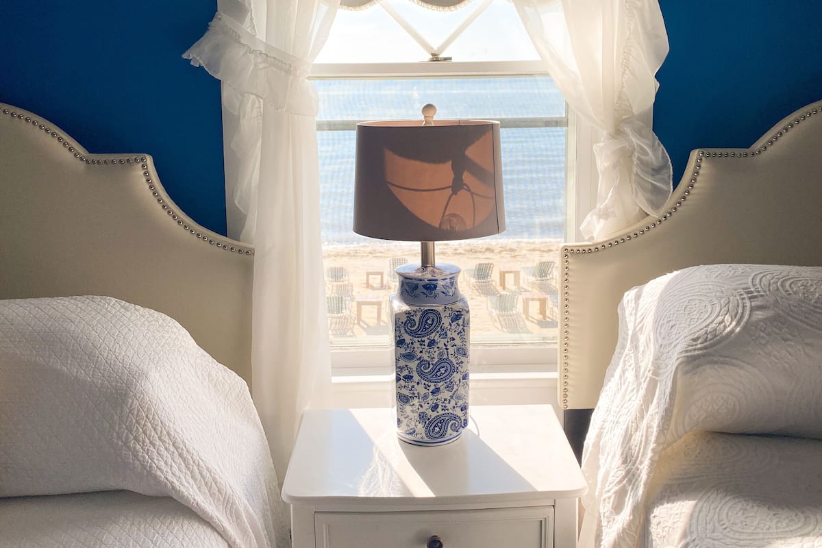 Een kamer met twee bedden, een nachtkastje met een lamp en een raam met dunne gordijnen.