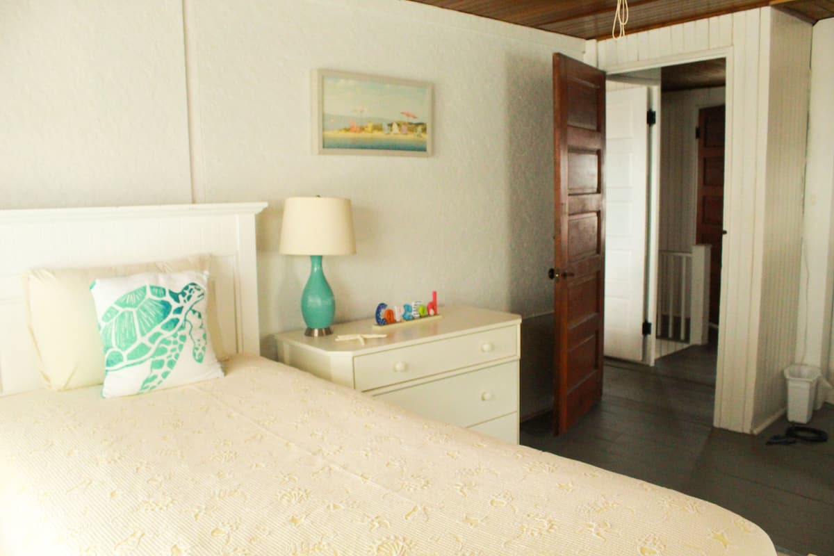 Een slaapkamer met een bed, een nachtkastje, een lamp en een deur naar een andere kamer.