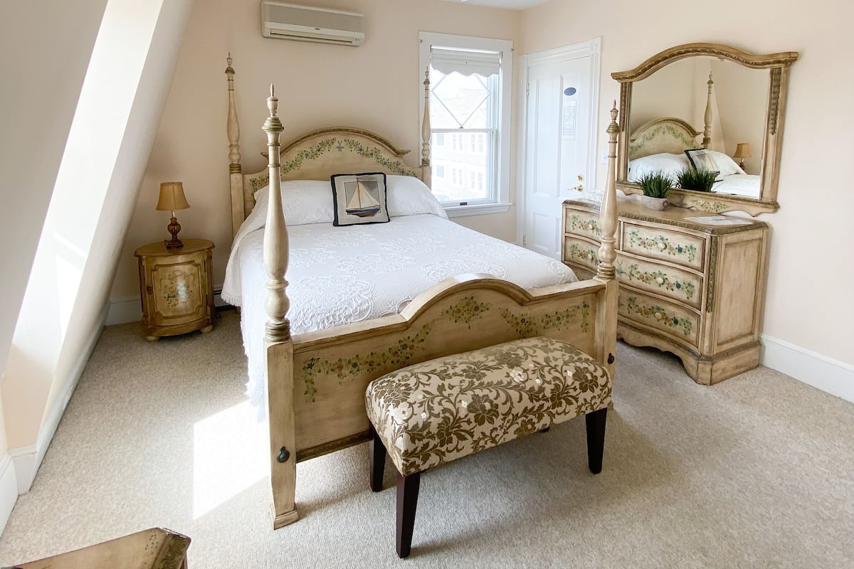 Een slaapkamer met een groot bed, een dressoir, een bankje, een plafondventilator en een raam.
