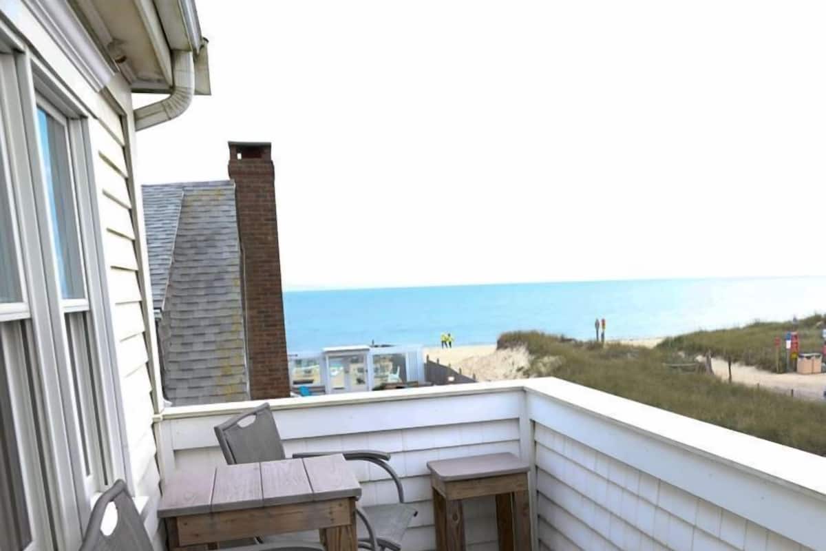 Een balkon met een tafel en stoelen, met uitzicht op een strand en de oceaan.