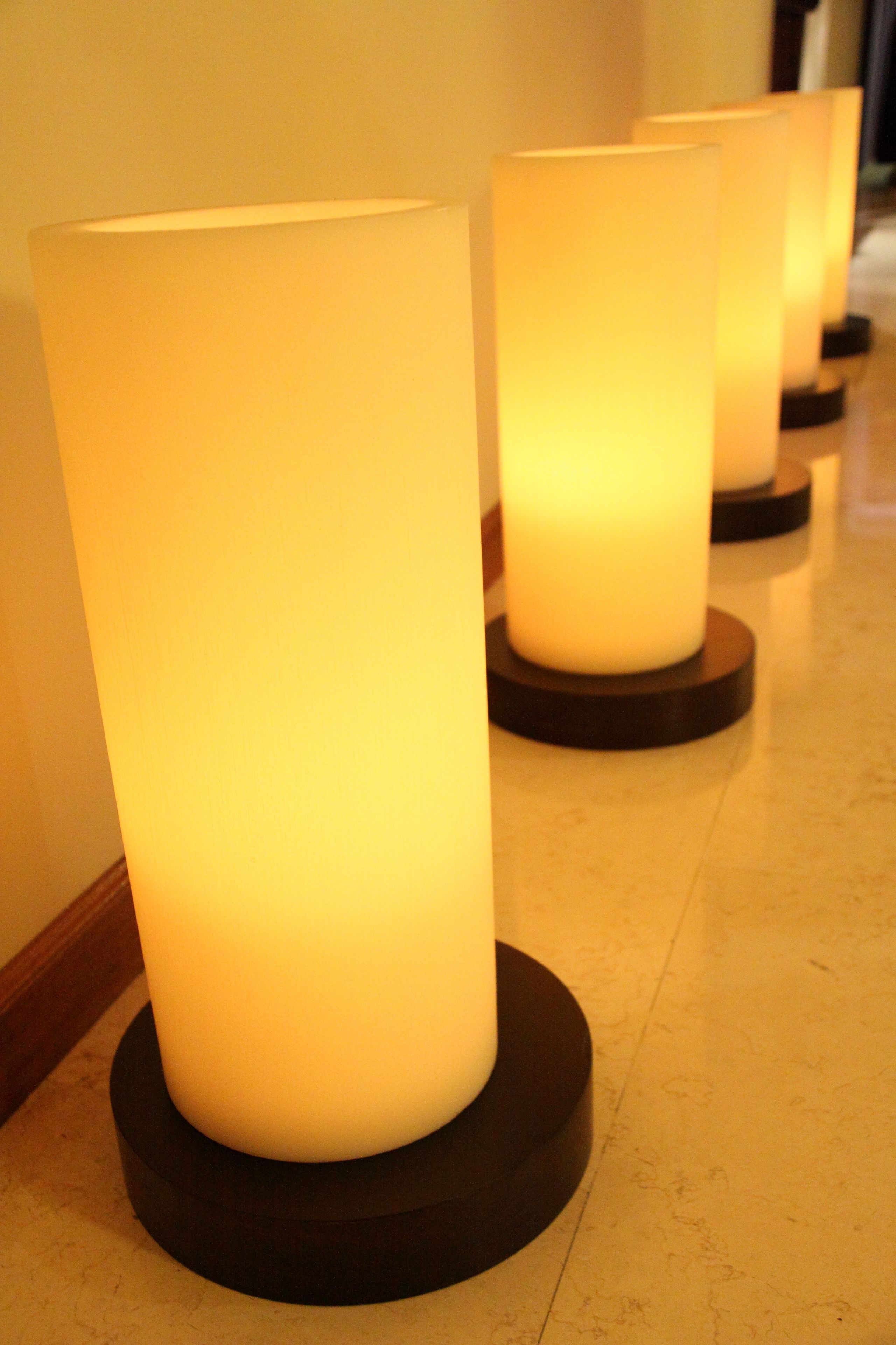 A row of cylindrical lamps with a warm glow, placed on circular bases, likely in a hotel lobby or similar public space.
