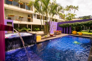 Ein Pool mit Wasserspiel, umgeben von einem Gebäude mit Balkonen und Bepflanzung.