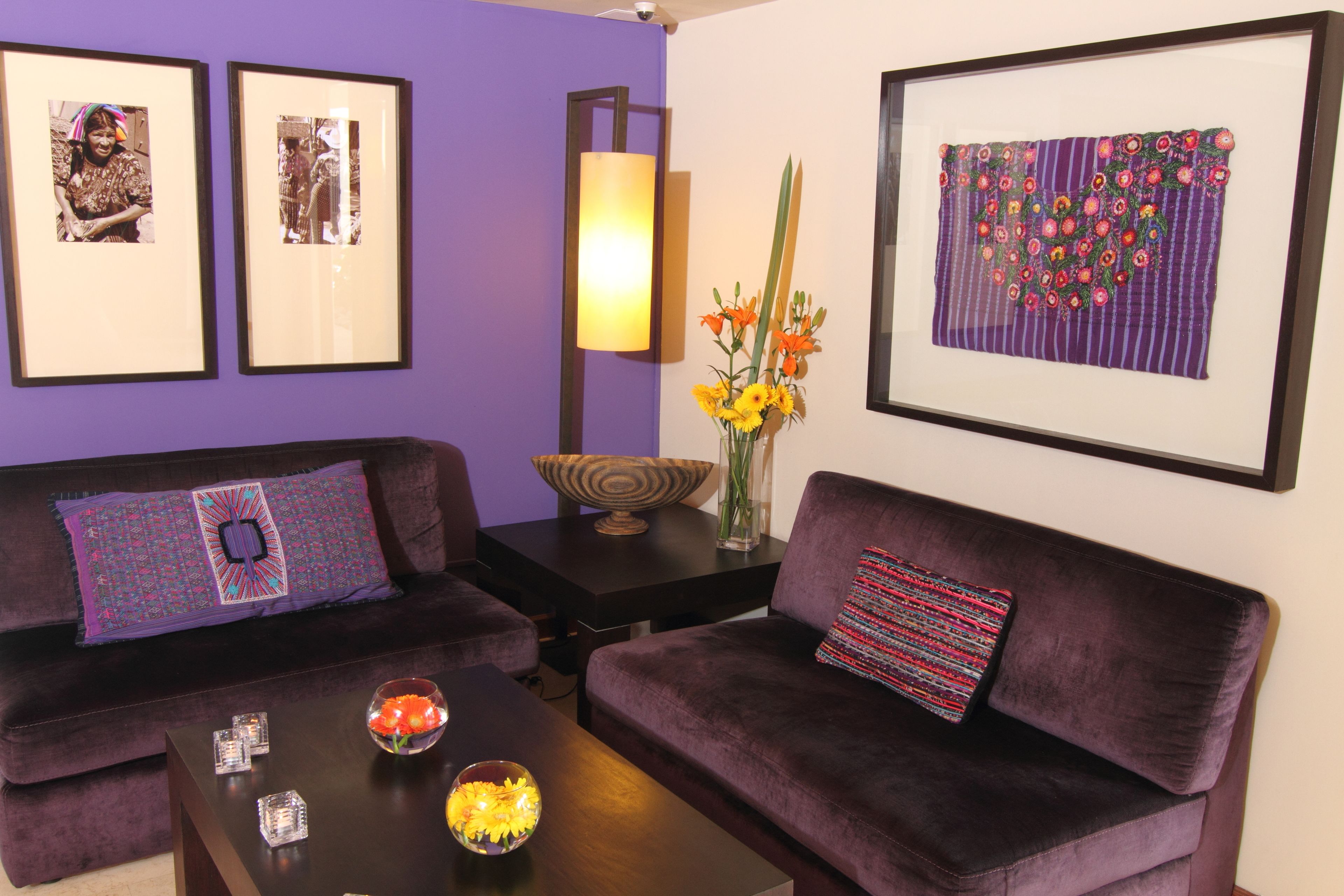 Ein Wohnzimmer mit zwei violetten Sofas, einem Couchtisch mit Dekoration, gerahmten Kunstwerken an den Wänden und einer Vase mit Blumen.