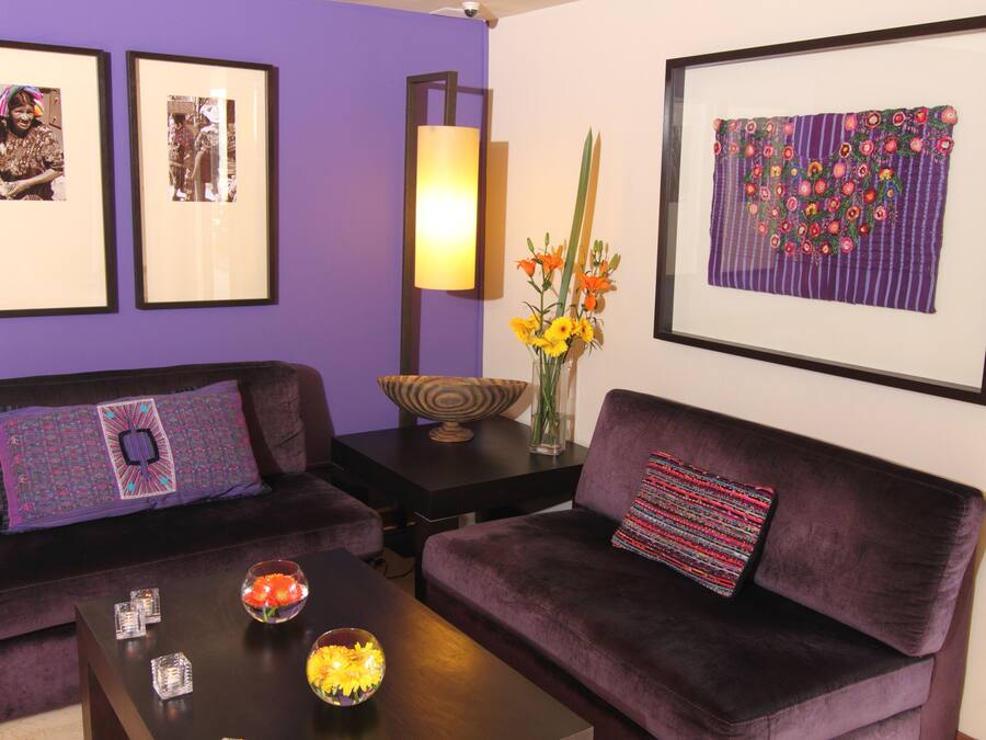 Ein Wohnzimmer mit zwei violetten Sofas, einem Couchtisch mit Dekoration, gerahmten Kunstwerken an den Wänden und einer Vase mit Blumen.