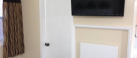 A room with a white door, a mounted flat-screen TV, and a whiteboard.