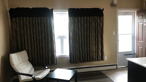 Una habitación con una silla, una mesita y un ventanal con cortinas.