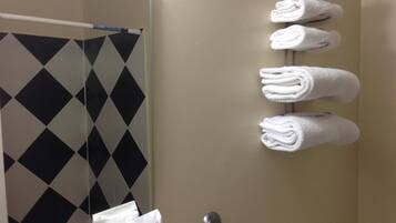 A bathroom with a shower curtain featuring a black and white diamond pattern, a towel rack with neatly folded towels, and a white bag hanging on the wall.