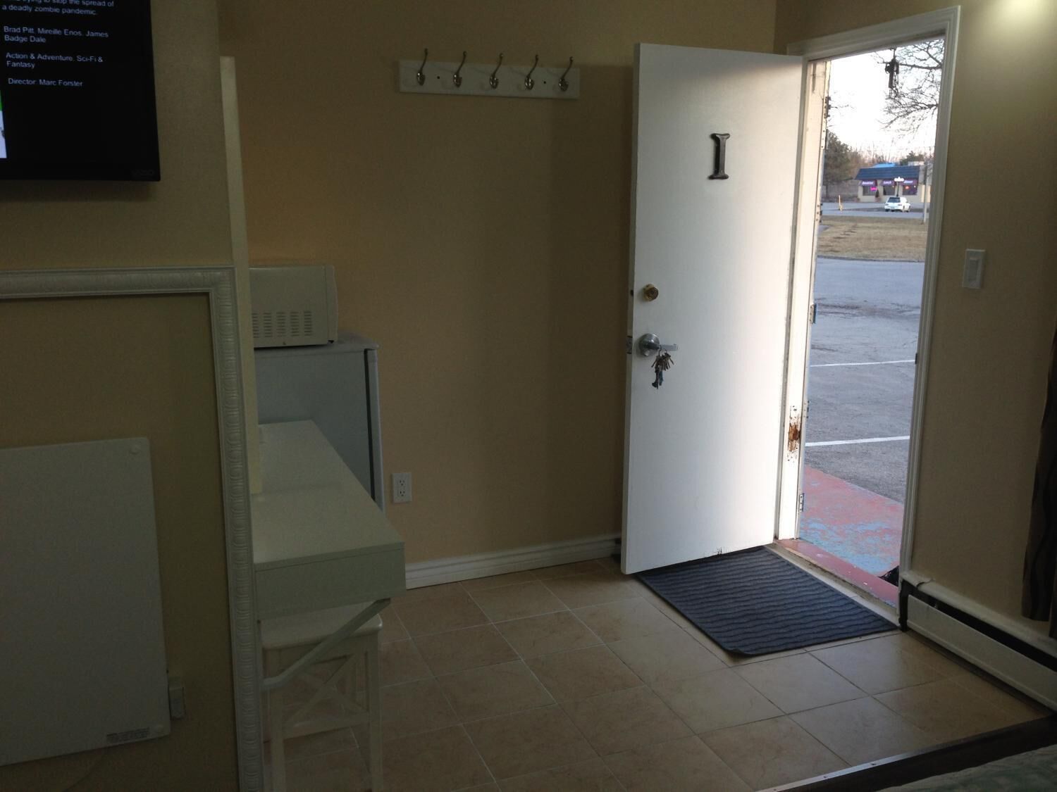 A room with a white door marked with an 'I', a white cabinet, a small table, and a wall-mounted TV displaying text.